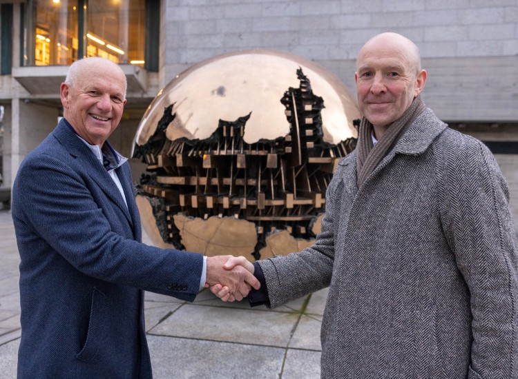 Two men shake hands before a spherical sculpture