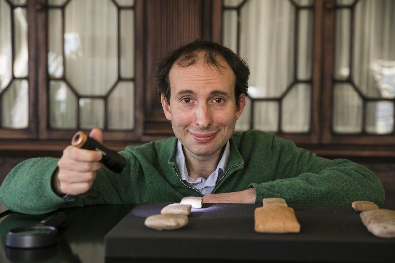 A man is leaning on a wooden table that displayed some ancient tablet artefacts