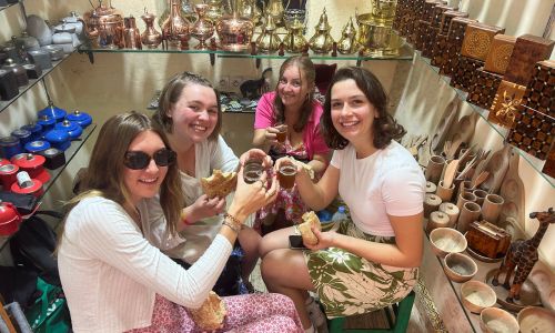 Four young woman in a group sitting and smiling holding small cups of mint tea