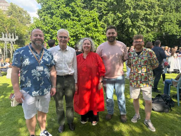 Photo of Linda with four members of the Trinity LGBT+ Staff Network committee. They are standing for a photo in the Provosts garden. There are trees in the background.