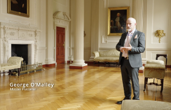 Photo taken in the Provost's Saloon with a man standing to the right of the frame. Overlaid text reads 'George O'Malley, Master Plasterer.'