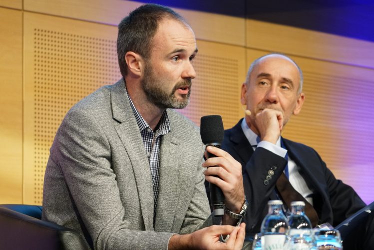 Assistant Professor John Gallagher giving an overview of his team’s solution for the ‘Materials for Clean Air’ Prize (back, Jean-Eric Paquet (centre), Director-General for Research & Innovation in the European Commission (©Roman Zach-Kiesling).