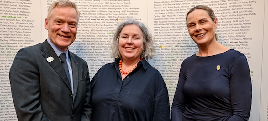Three people standing and smiling in front of a banner