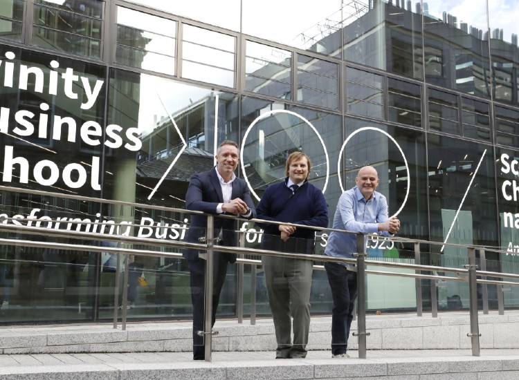 Three men pose outside modern building