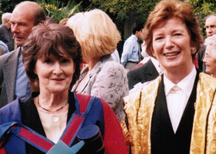 Two women pose in graduation robes