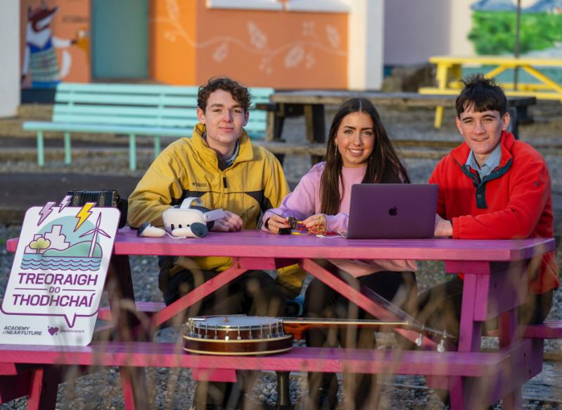 Three teenage students sitting on a bench with a Treoraigh do Thodhchaí sign on display.