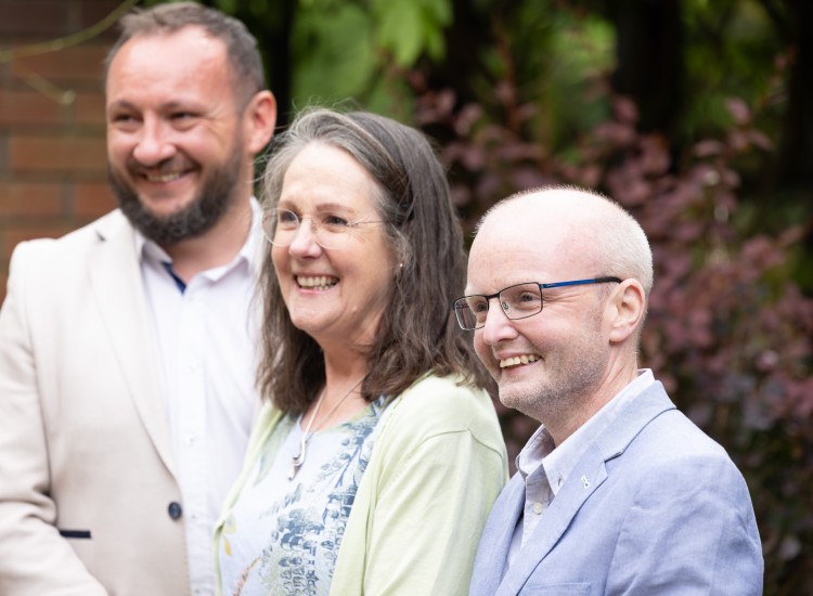 Three people pictured in a garden, smiling