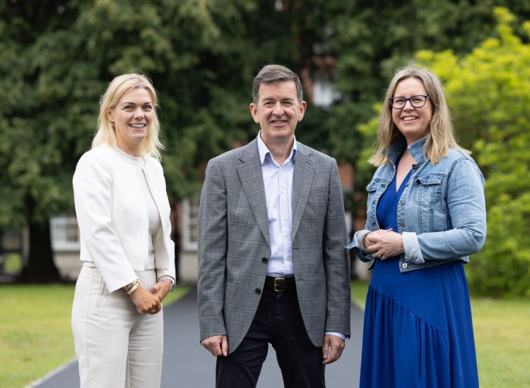 Two women and a man pose against a leafy background