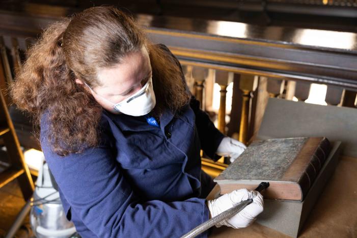 Project assistant Patricia Bedlow vacuums a book in Old Library