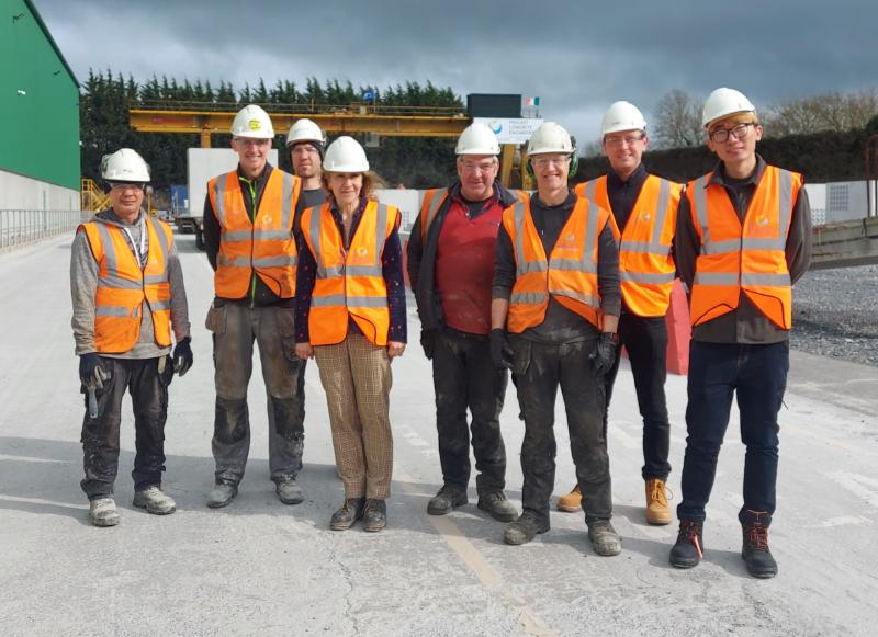 Researchers and engineers in orange hi-vis jackets and white hard hats outside a factory. Prof. Sara Pavia is in the centre.