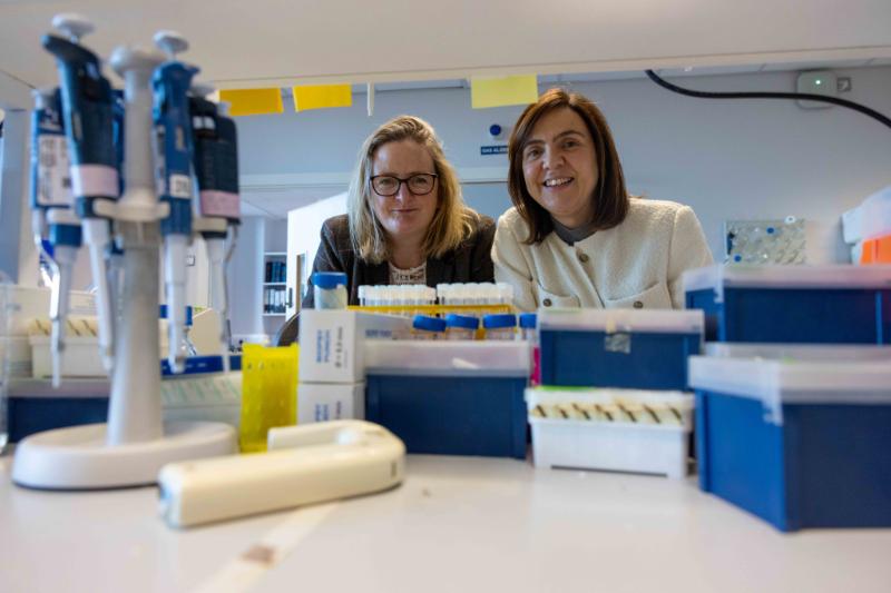 Prof. Ruth Massey and Prof Rachel McLaughlin look through shelving on a research bench in Rachel's laboratory in the Trinity Biomedical Sciences Institute.