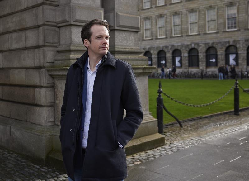 Tomas Ryan wearing a dark coat in Trinity, standing beneath the campanile
