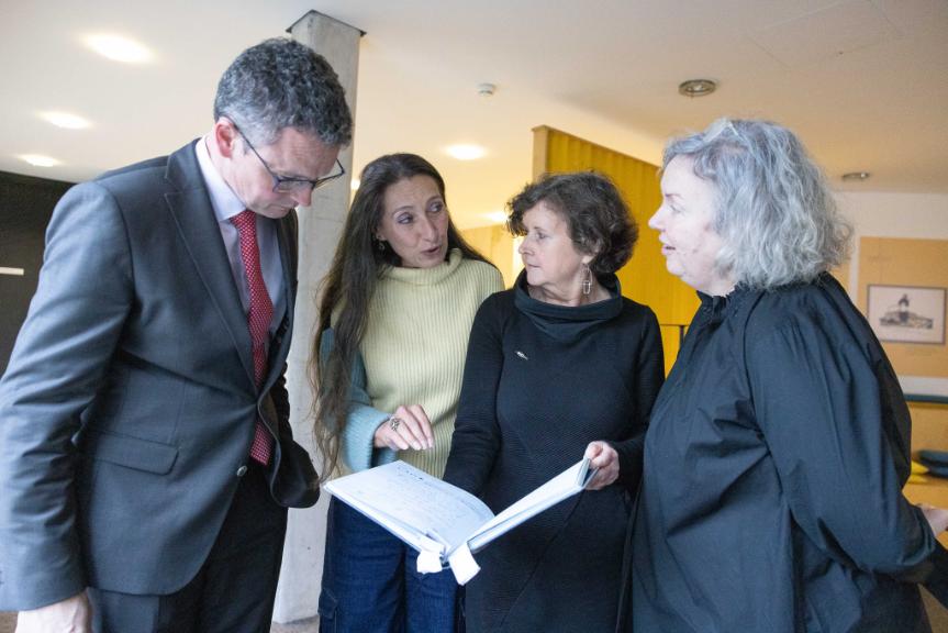 One man and three women looking at a book