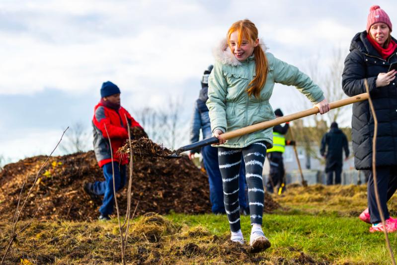 Children move leaves and carry sapling before planting them in Darndale.