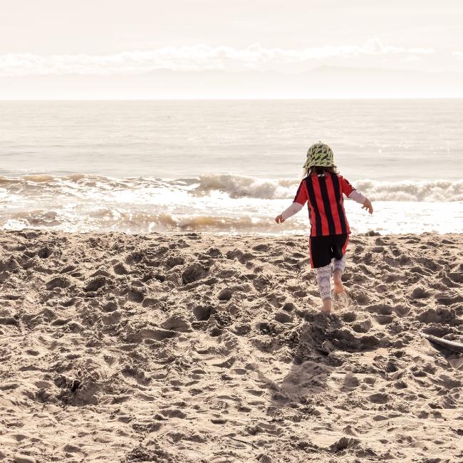 A child running on the sand by the sea on a sunny day