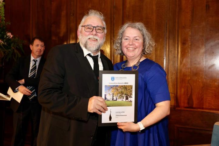 Professor Werner Blau, in a black suit, receives the Lifetime Achievement Award from Provost Linda Doyle.