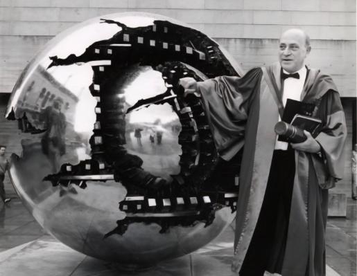 Man in robes beside sphere sculpture